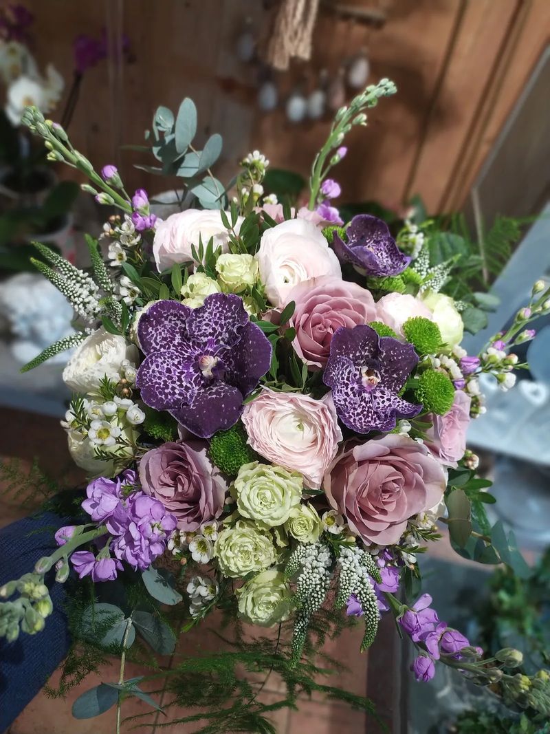 Bouquet rond d'orchidées Vanda violettes, de roses mauves et de renoncules blanches, tenu à la main dans la boutique