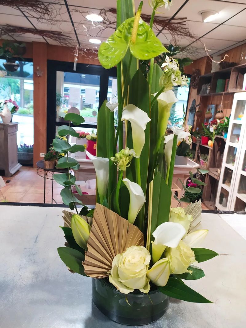 Composition haute d'arums blancs, d'anthurium vert et de palme séchée, posée sur le comptoir de la boutique