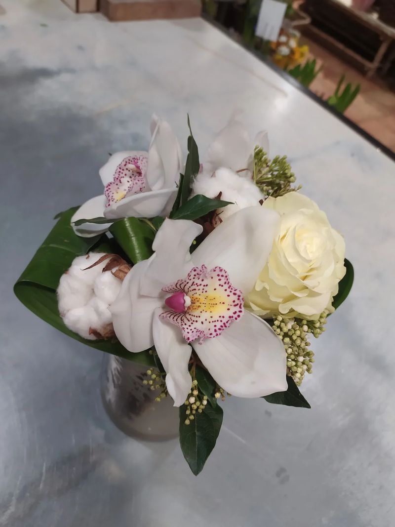 Vue de dessus d'une composition d'orchidées cymbidium, de coton et de viorne, posée sur le plan de travail de l'atelier