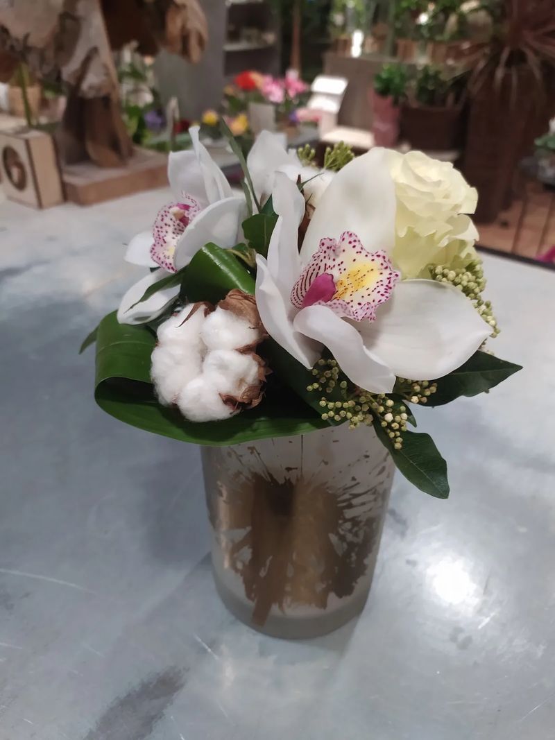 Composition d'orchidées cymbidium blanches, de branches de coton et de viorne dans un vase mercurisé