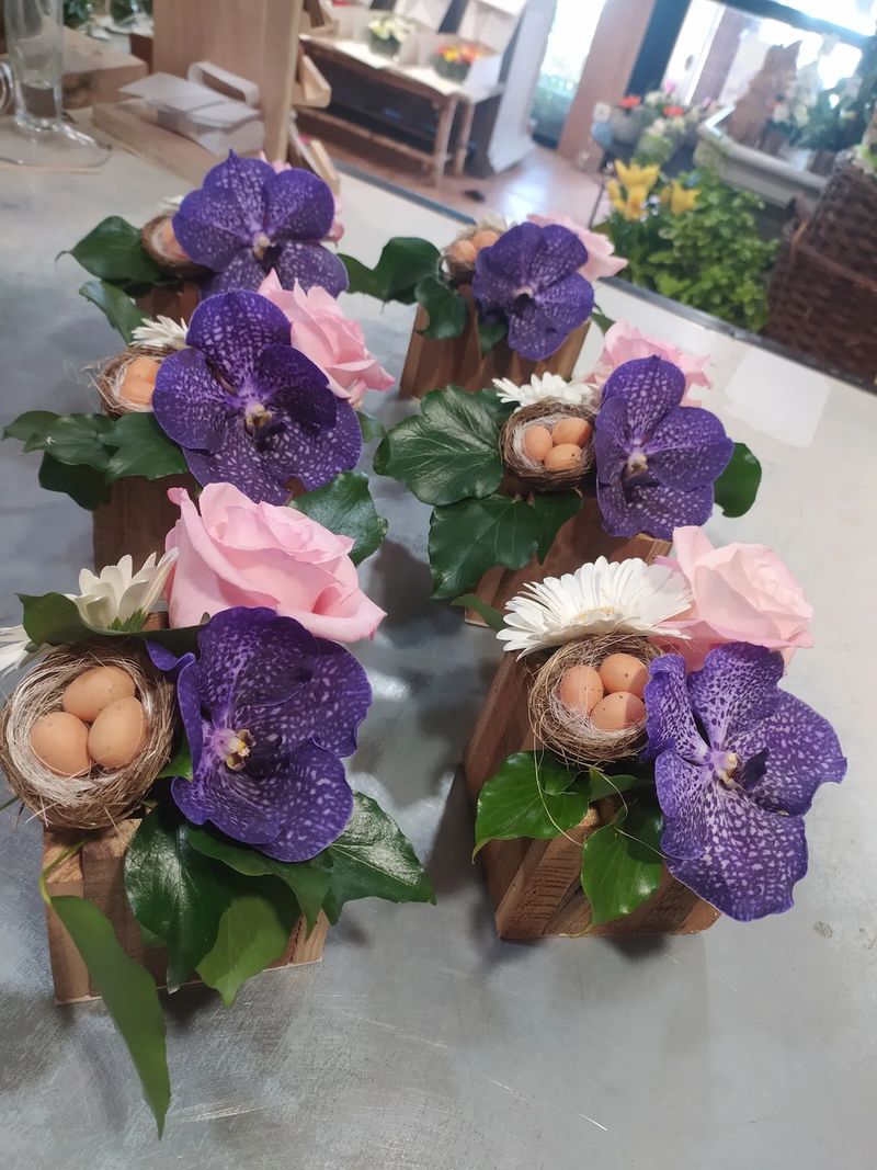 Série de petites compositions de Pâques en cagettes de bois, avec orchidées Vanda violettes, roses roses et nids garnis d'œufs